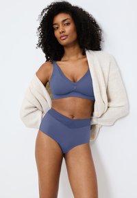 Modrá bezšvová podprsenka a vysoké kalhotky vyrobené z hladkého materiálu, doplněné o světle béžový pletený kardigan. Nastavitelné ramínka na podprsence.
