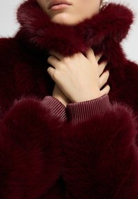 Burgundský límec z umělé kožešiny s jemnou texturou, vrstveným designem, žebrovanými manžetami svetru a pevným držením ruky na krku.