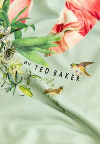Gai zaļš audums ar ziedu rakstu, kurā ir rozā ziedi, zaļas lapas un putni, kā arī melna uzraksta "by TED BAKER".