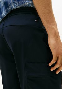 Pantaloni cargo blu navy realizzati in tessuto liscio, dotati di una vita elastica e tasca laterale, con un piccolo logo decorativo.