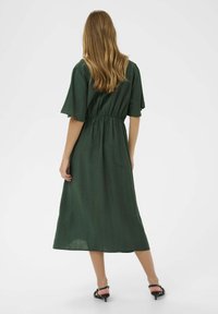 Rochie verde, de lungime medie, cu mâneci scurte și late și talie elastică. Fabricată dintr-un material ușor, având o textură netedă și un design simplu.