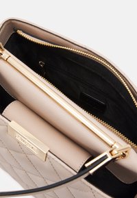 Beige håndtaske med tekstureret læder, guld lynlås og sort foer. Har en kviltet overflade og et indvendigt lomme til opbevaring.