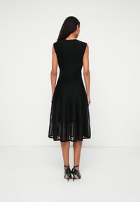 Μαύρο φόρεμα με εφαρμοστό μπούστο και αέρινη, πλισέ φούστα. Υφασμάτινη επιφάνεια με κατακόρυφες ρίγες, χωρίς μανίκια και μήκος μέχρι το γόνατο.