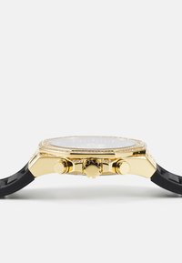Orologio dorato con quadrante grigio, dettagli in cristallo e cinturino in gomma nera. Presenta tre pulsanti e una corona sul lato.