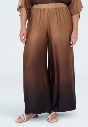 Pantalones anchos de pierna ancha en degradado marrón con cintura elástica, usados con sandalias por una persona de pie contra un fondo liso.