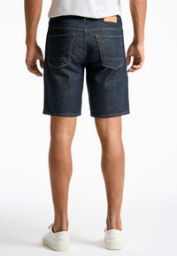 Dunkelblaue Jeansshorts mit geradem Schnitt, ausgestattet mit zwei Gesäßtaschen und einem Lederpatch am Bund. Strukturierter Stoff, lässiger Stil.