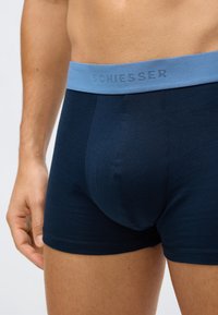 Male torso wearing navy blue boxer briefs with a light blue waistband labeled "Schiesser," standing against a plain background.