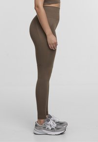 Brown high-waisted leggings made of stretchy fabric, featuring a fitted design and seamless sides. Worn with gray athletic shoes.