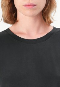 Svart kortermet topp med rund hals. Glatt stoff med synlige sømmer langs kragen. Tettsittende design.