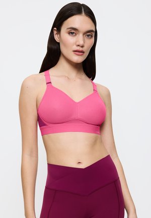 Różowy biustonosz sportowy z teksturowanym wzorem, regulowanymi ramiączkami i szerokim pasem. W połączeniu z bordowymi legginsami z wysokim stanem.
