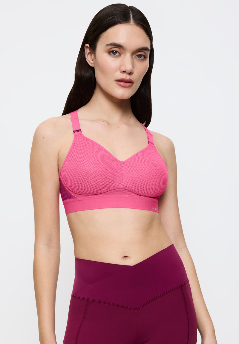 Różowy biustonosz sportowy z teksturowanym wzorem, regulowanymi ramiączkami i szerokim pasem. W połączeniu z bordowymi legginsami z wysokim stanem.