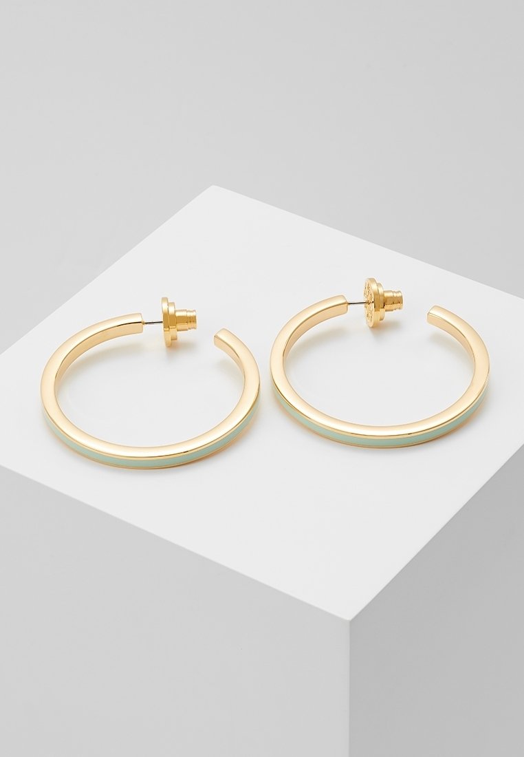 Paire de boucles d'oreilles créoles dorées avec une fine bande en émail bleu clair, présentée sur une surface blanche inclinée.