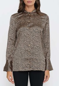 Blusa in stampa leopardata realizzata in tessuto satinato, con apertura a bottoni, colletto e maniche svasate. I colori predominanti sono il beige e il nero.