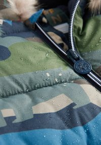 Water-resistant puffy jacket in green, blue, and beige camouflage pattern. Features zippers and visible water droplets on fabric texture.