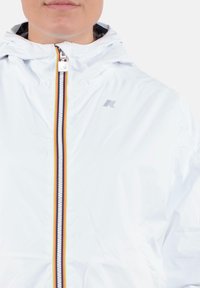 Giacca leggera bianca con zip frontale, decorata con accenti a righe multicolori e cappuccio. Logo visibile sul lato sinistro.