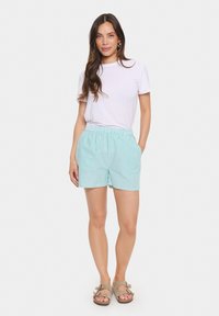 Pantaloni corti a righe blu chiaro con cintura elastica e tasche laterali, abbinati a una t-shirt bianca semplice e sandali beige.