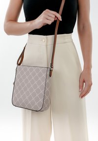 Beige Umhängetasche mit einem Rautenmuster, ausgestattet mit einem braunen Ledertragegurt und schwarzen Kanten. Glatte Textur mit strukturierter Form.