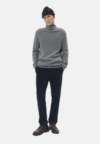 Sivi rebrasti turtleneck pulover, tamnoplave kord čarape, smeđi cipele i crna pletena kapa nošena malo na stranu.