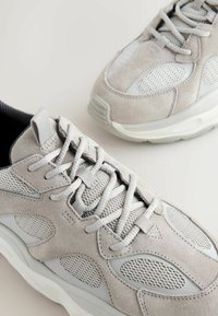 Hellgraue Sneakers aus Wildleder und Mesh, mit schnürbarem Design, gepolsterter Zunge und strukturierten Akzenten an den Seiten.