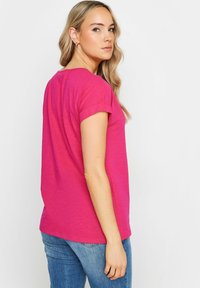 T-shirt rosa a maniche corte con una vestibilità morbida, texture soffice e maniche arrotolate, abbinato a jeans blu. Design semplice, senza fantasie.