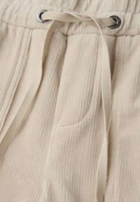 Beige Rippstoff-Jogginghose mit einem elastischen Bund und einer beigen Kordel, die durch metallene Ösen gefädelt ist.