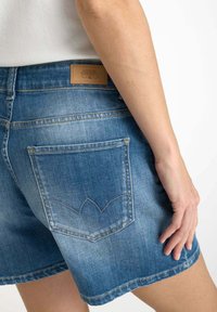 Denimshorts in een lichtblauwe wassing, met een achterzak en decoratieve stiksels. De tailleband heeft een leren label in bruin.