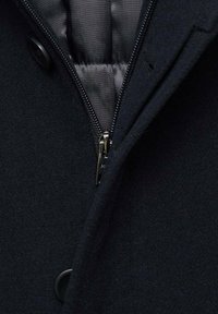 Svart ullkappa med dragkedja, slät inredning och runda knappar. Texturerad utsida, skräddarsydd design, elegant finish.