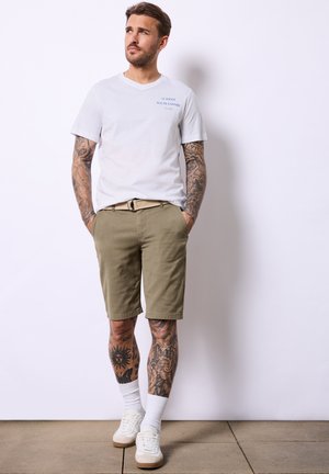 Herretøj med en hvid V-hals t-shirt med blå tekst, khaki shorts og hvide sneakers parret med hvide sokker.