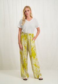 Witte v-hals t-shirt gecombineerd met losse, lichtgrijze broek met een levendig geel abstract patroon en een trekkoord in de taille. De broek heeft zijzakken.