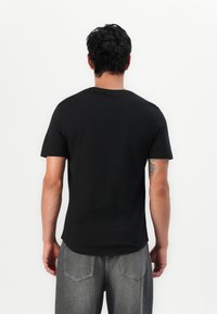 Black t-shirt made of cotton, short sleeves, round neckline, and a relaxed fit. Worn with gray denim jeans.