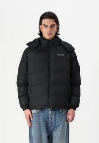 Μαύρο μπουφάν με ψηλό γιακά, κλείσιμο με φερμουάρ και ελαστικούς καρπούς. Διαθέτει λογότυπο στο αριστερό στήθος και κουκούλα με αποσπώμενη λειτουργία.