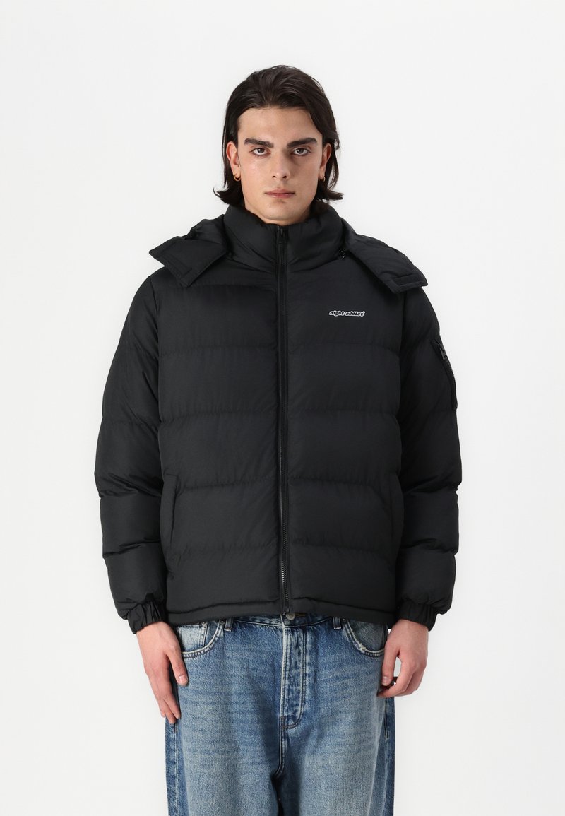 Μαύρο μπουφάν με ψηλό γιακά, κλείσιμο με φερμουάρ και ελαστικούς καρπούς. Διαθέτει λογότυπο στο αριστερό στήθος και κουκούλα με αποσπώμενη λειτουργία.