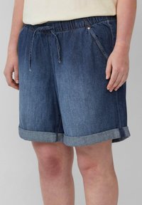 Shorts en denim bleu avec une taille élastique et un cordon de serrage. Caractéristiques : ourlets roulés et poches latérales. Le matériau est texturé et durable.