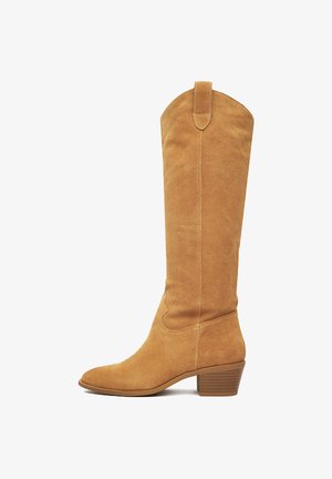 Vysoká béžová zamšová čižma s okrúhlym špičkou, stredne vysokým hromadným podpätkom a pútkom na vrchu holenice na bielom pozadí.