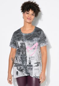 Camiseta gris de manga corta con estampado de paisaje urbano y acento rosa en el centro, con escote redondo, combinada con leggings burdeos.