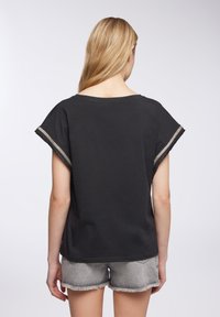 Top corto nero a maniche corte con una vestibilità comoda, caratterizzato da un ampio scollo e rifiniture strutturate sulle maniche. Abbinato a bermuda grigi sfondata.