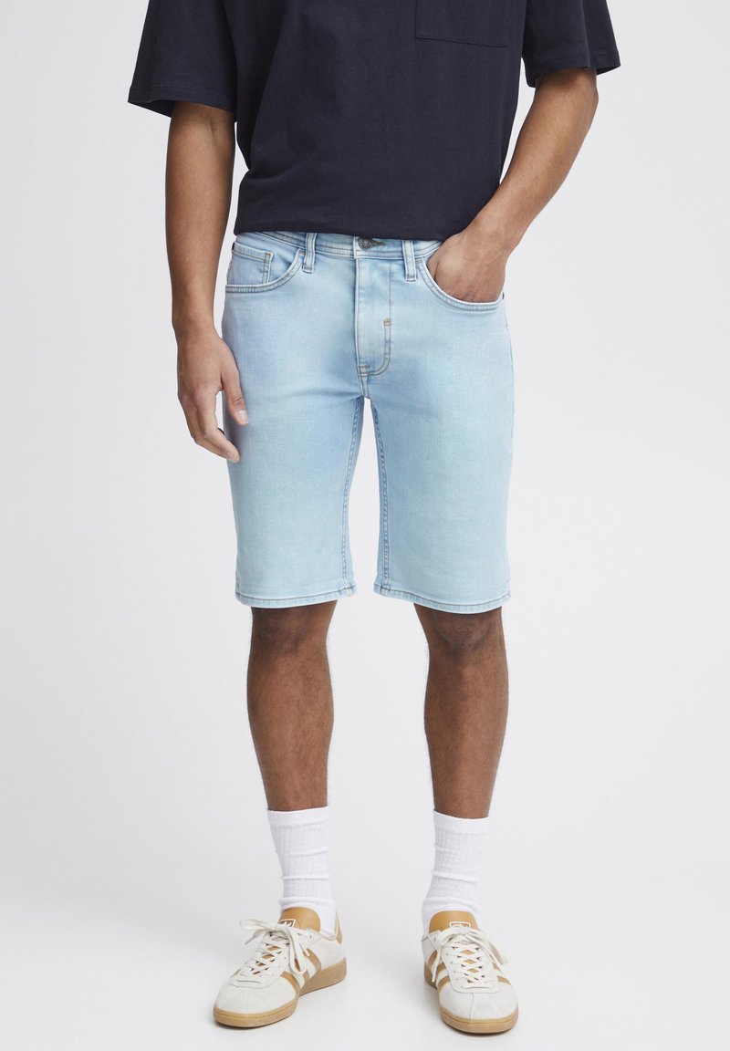 Shorts de mezclilla en un azul claro con corte recto, cinco bolsillos y un ligero desvanecimiento. Combinados con una camiseta azul marino y calcetines blancos.