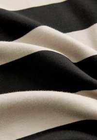 Tissu en coton avec des rayures horizontales noires et crème, présentant une texture douce et une surface légèrement en relief, affichant de douces plis.