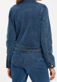 Dark blue denim jacket with a fitted design, long sleeves, and a buttoned cuff. Features visible stitching and a banded waistline.