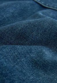 Gros plan sur un tissu en denim bleu texturé avec un tissage visible et des coutures sur les sections pliées.