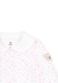 Blusa bianca con colletto rotondo, decorata con piccoli fiori rosa. Presenta un ricamo di un orsetto sulla manica sinistra.