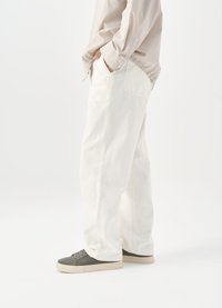 Λευκά, φαρδιά τζιν παντελόνια από ντένιμ. Διαθ�έτουν βαθιές τσέπες και διακριτική ραφή. Συνοδεύονται από γκρίζα παπούτσια σε απλό φόντο.