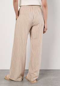 Pantalons à rayures beiges à jambes larges avec une taille élastique, dotés de poches latérales et d'une texture de tissu léger.