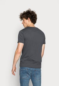 Graues Kurzarm-T-Shirt mit Rundhalsauschnitt. Glattes Baumwollmaterial, taillierte Passform, ohne sichtbare Muster. Kombiniert mit blauen Jeans.