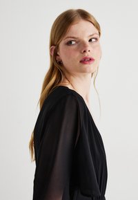 Black dress with sheer sleeves and a V-neck design. Fabric appears lightweight, smooth texture, cinched at the waist, simple and elegant.