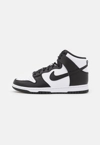 Sneakers alte con un design in pelle bianca e nera, dotate di punta perforata, chiusura con lacci e suola in gomma. Logo Nike in evidenza.