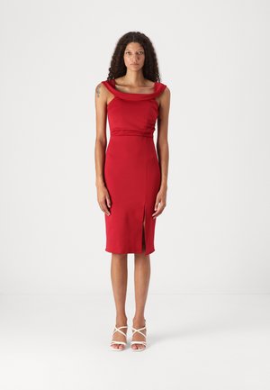 Red dress with a fitted silhouette, wide draped neckline, and side slit. Made from a smooth fabric. Paired with white strappy heels.