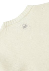 Nahaufnahme eines cremefarbenen Strickpullis, der den gerippten Rundhalsausschnitt und das kleine, gestickte graue Logo in der Nähe des Kragens zeigt.