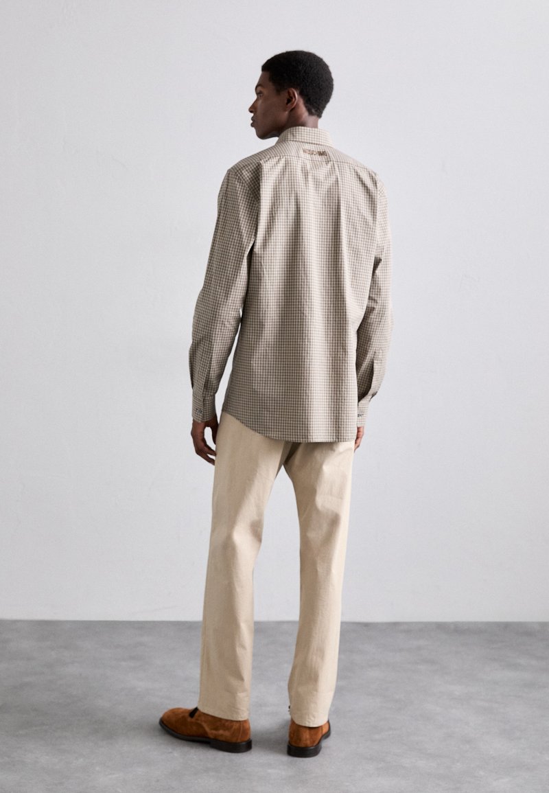 Hellbraunes kariertes langärmeliges Hemd mit Button-Down-Kragen, kombiniert mit hellbeigen Hosen und braunen Wildlederschuhen. Minimalistisches Design.