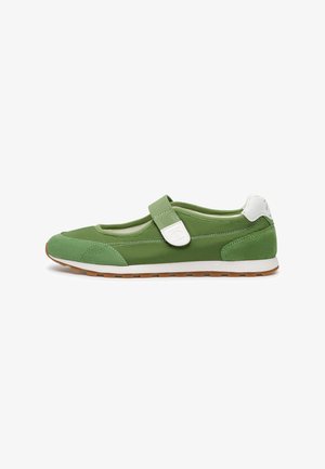 Zapatilla deportiva verde estilo Mary Jane con punta y talón de ante, tira blanca de Velcro, parche blanco en el talón y suela de goma color caramelo sobre fondo blanco.